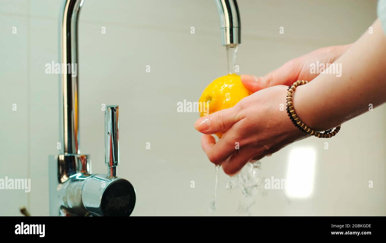 Close-up shot of woman's hands wash a lemon under the tap with water. Washing fruits before eating. Stock Photo