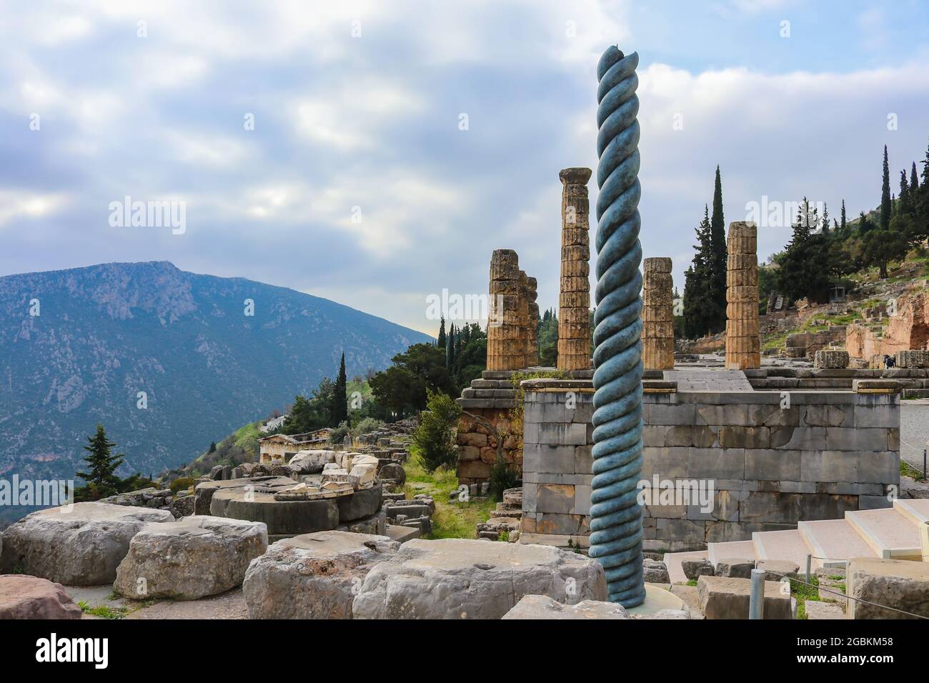 View of mountainside site of ancient Delphi Greece with twisted column in front of Temple of Apollo with a treasury down the hill and another mountain Stock Photo