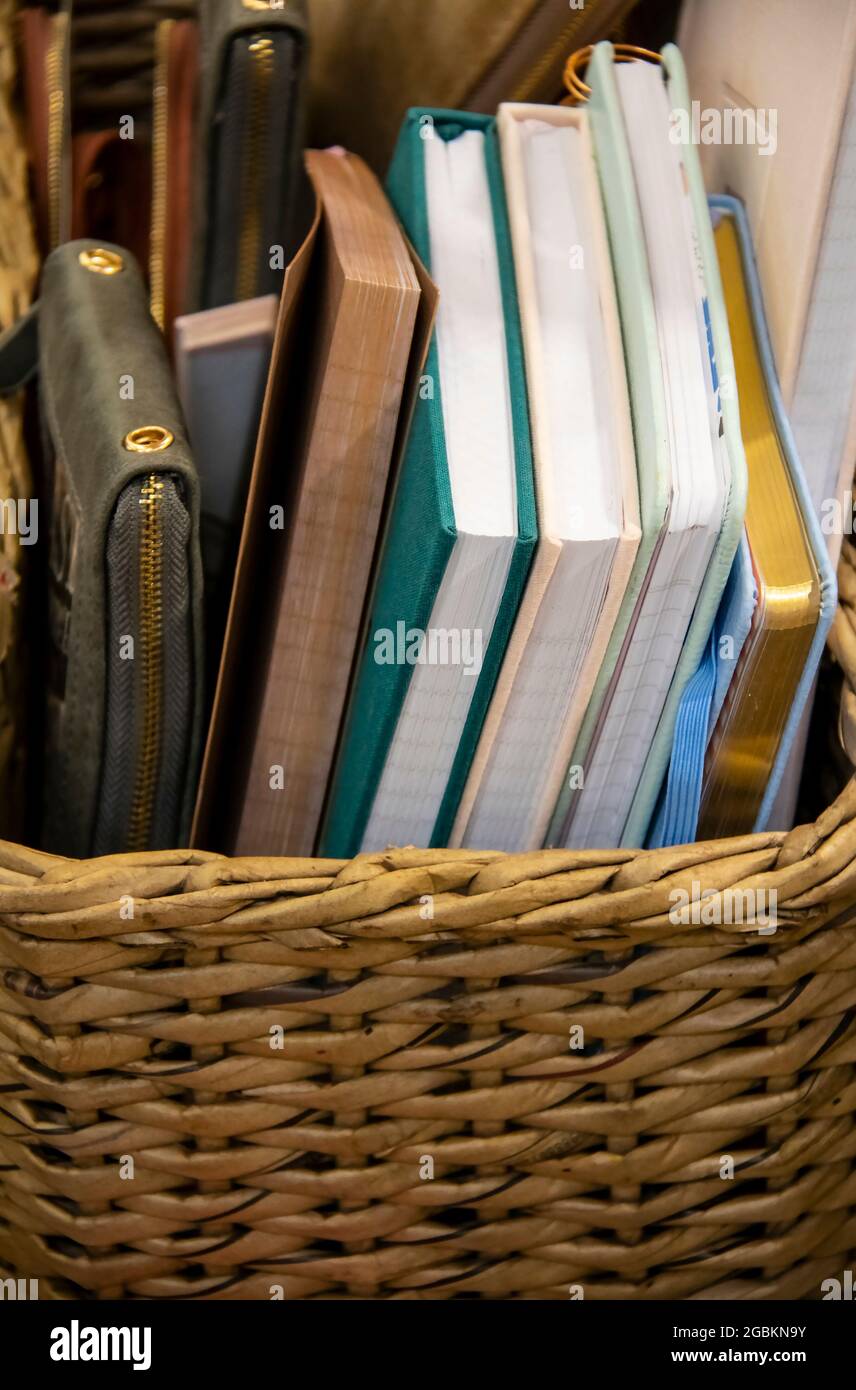 Assorted notebooks or books plus a notepad in a zip up cover in a woven basket Stock Photo