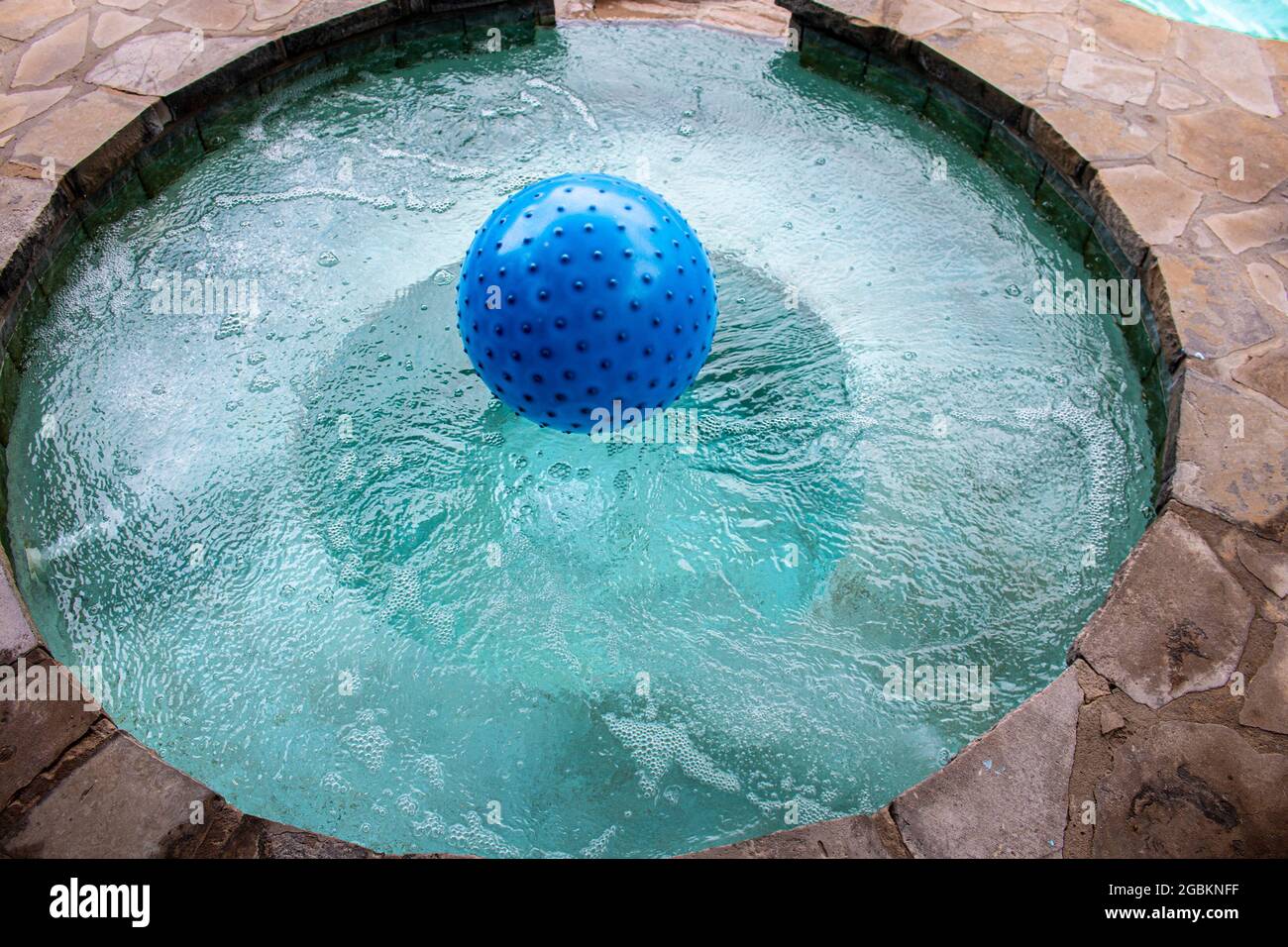 Bumpy blue beach ball floating in built-in hot tub in rock patio - top view Stock Photo