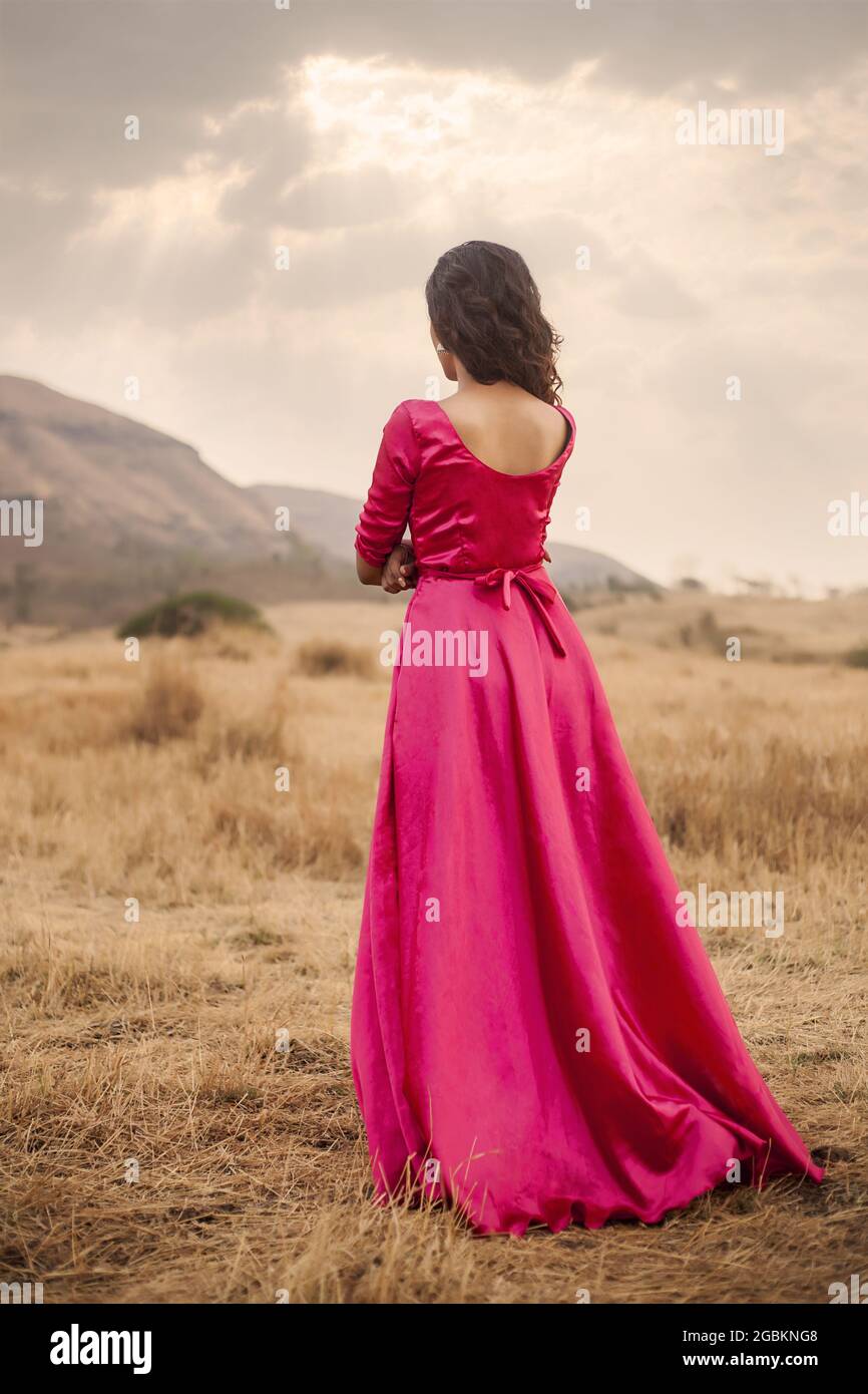 Vertical shot of a young Indian woman in a pink traditional dress, outdoors  facing the mountains Stock Photo