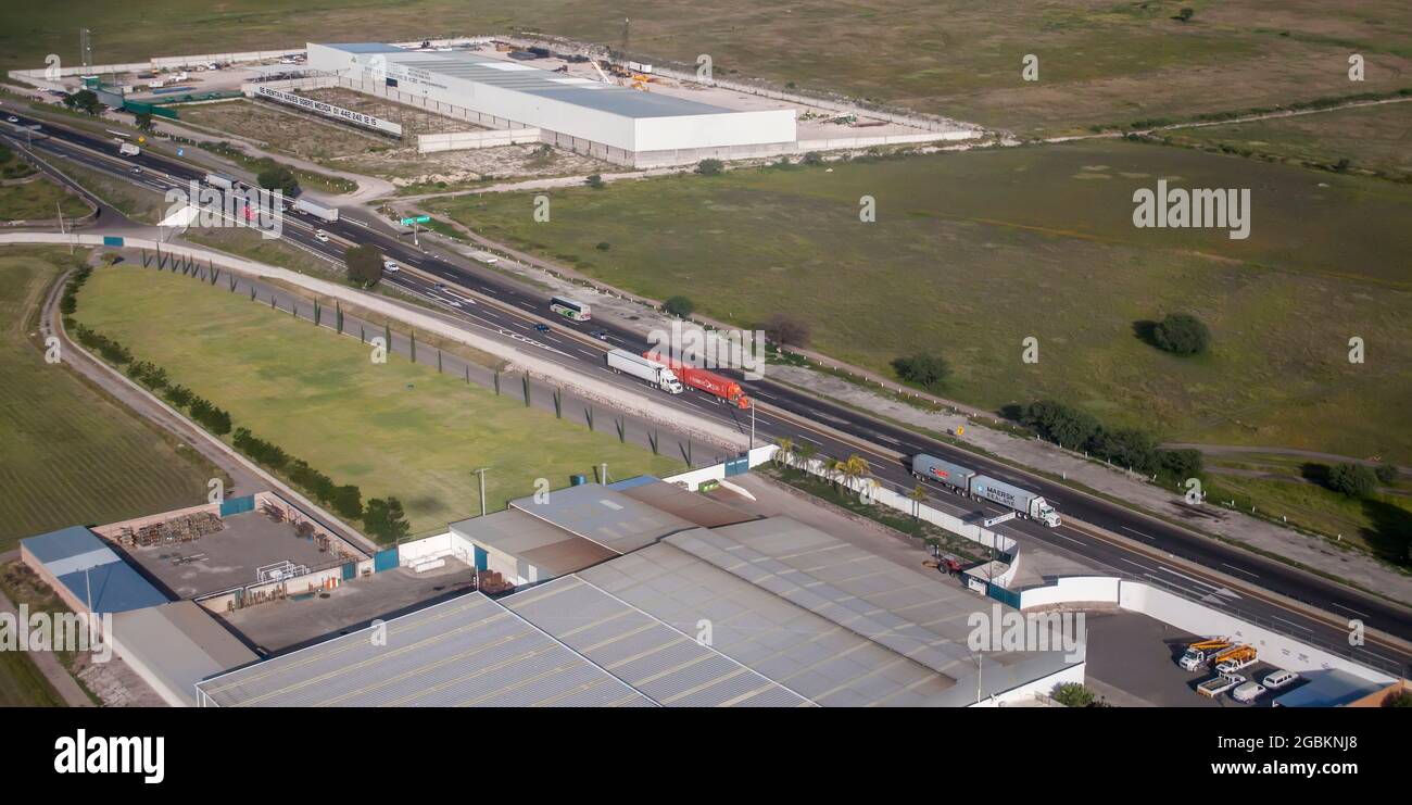 Trucks on highway pass by an industrial estate in central Mexico Stock Photo