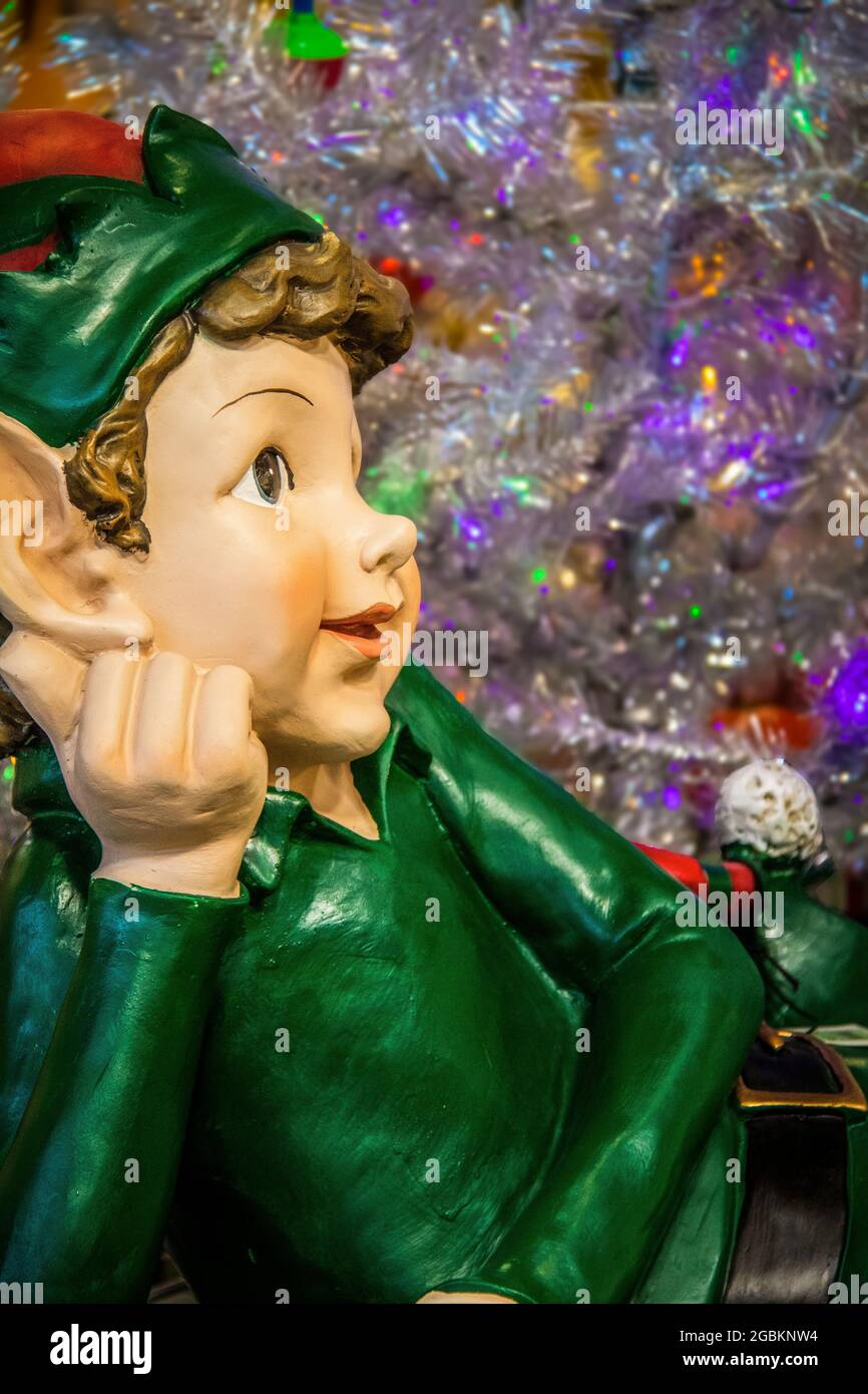 Cute elf figurine dressed in green relaxing in front of silver bokeh Christmas tree Closeup and selective focus Stock Photo