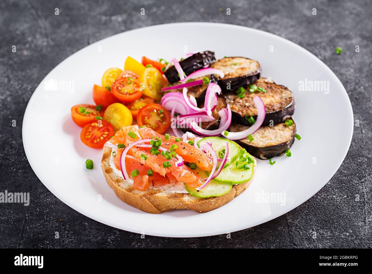 Delicious brunch  salmon  bread cream cheese sandwiches and arugula, tomatoes salad on a dark background. Stock Photo