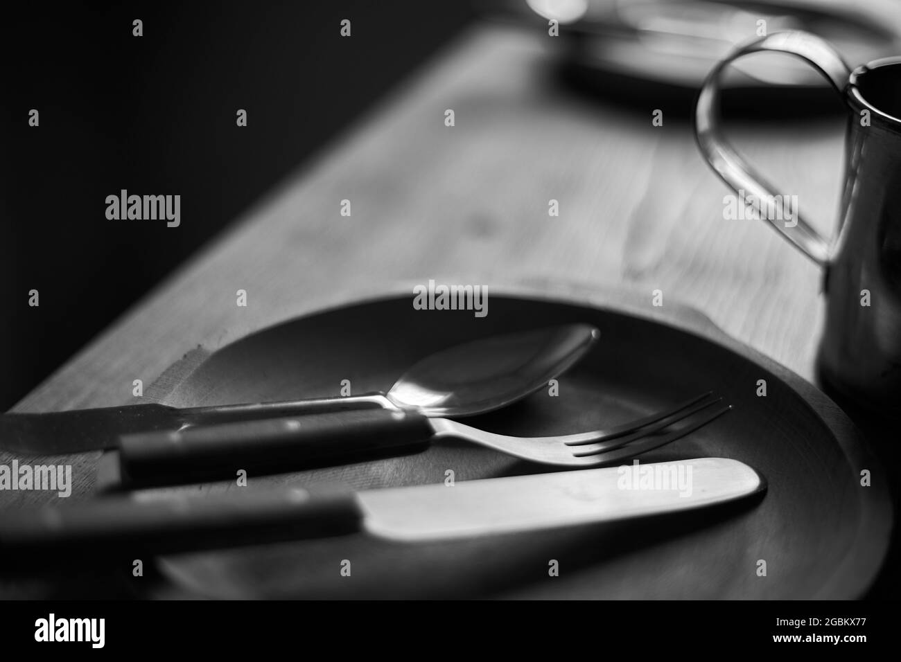 Trio. Spoon, fork and knife in the wooden plate. Defocused black and white background. Close up. Stock Photo