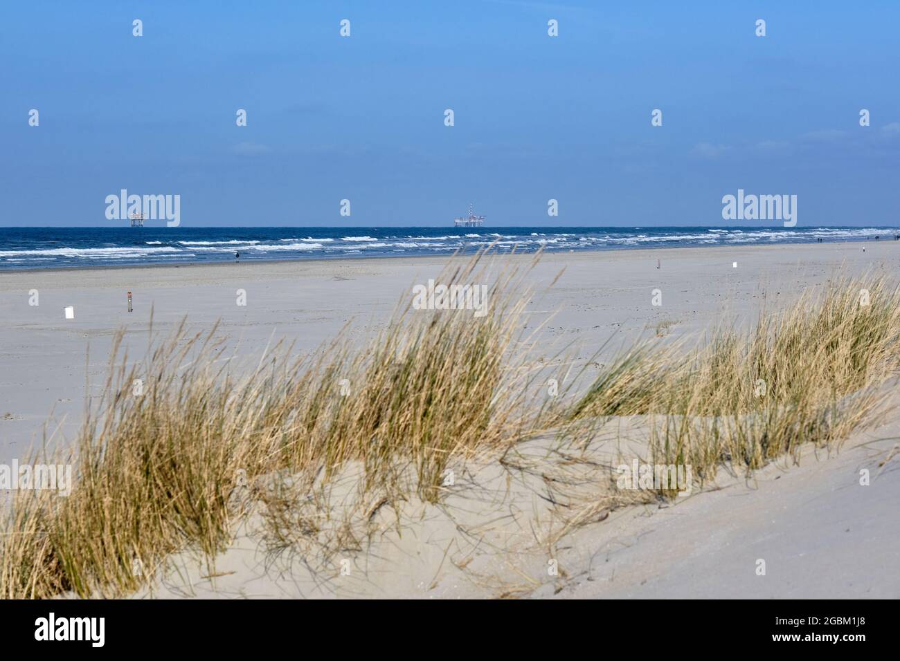 Ameland,Netherlands April 20,2021-Beach with offshore platform, sand, beach grass and surf. People walking on the beach. NAM, Oil rig. Natural gas Stock Photo