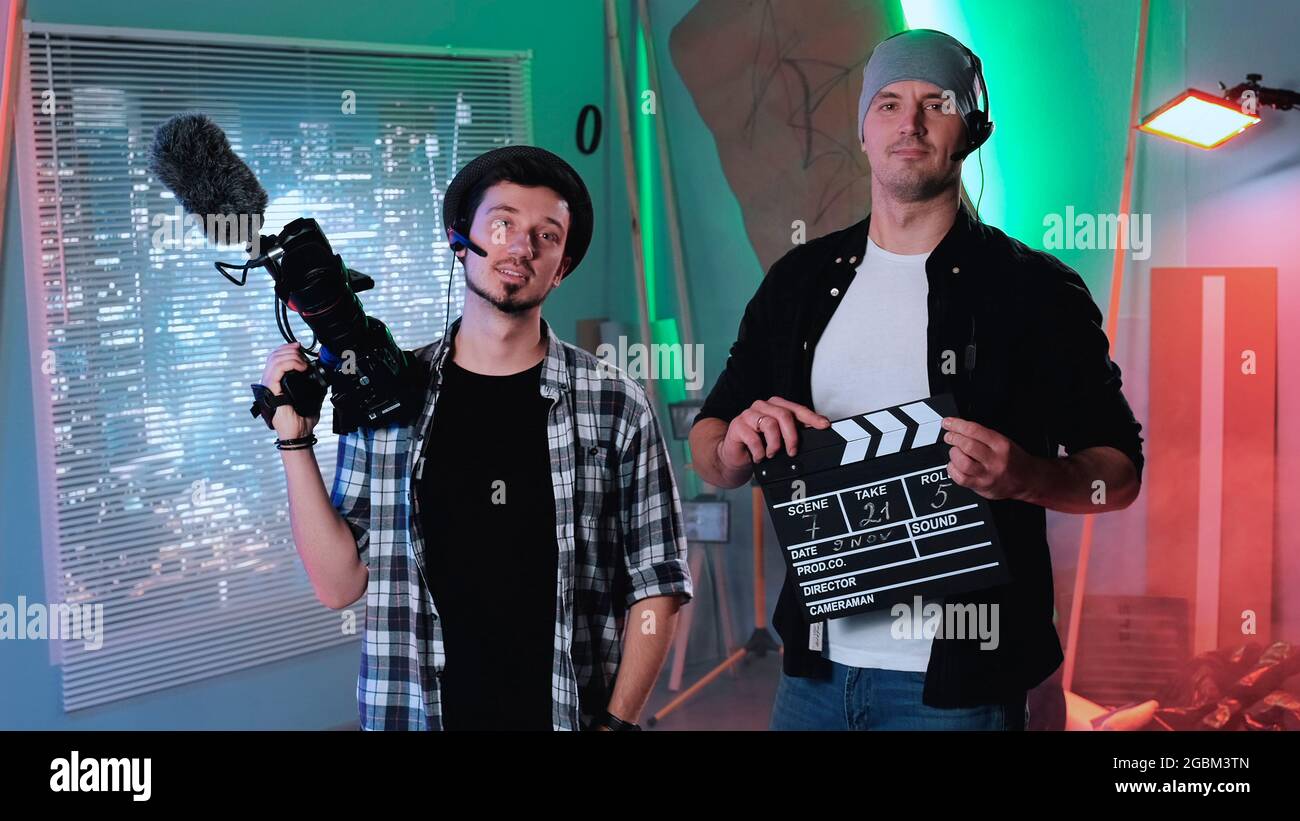 Camera man and producer assistant smiling to the camera and showing their equipment: movie camera and movie clapper board. Stock Photo