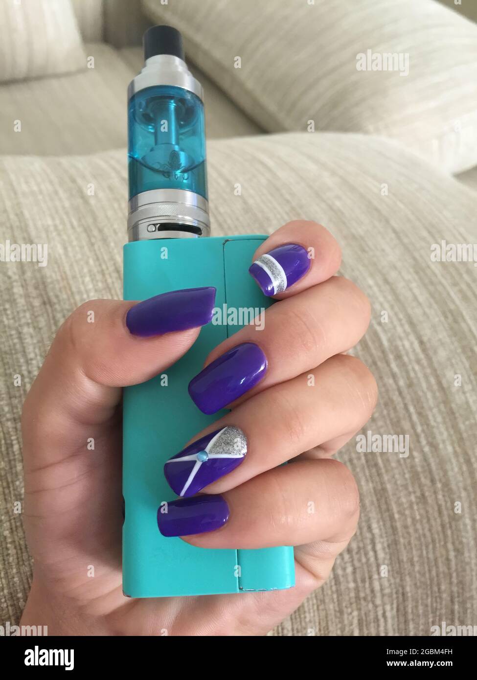 Female hand with gel polish holding VAPE close-up on sofa background. Woman's hands holding electronic cigarette. Nail art on hers nails. Stock Photo