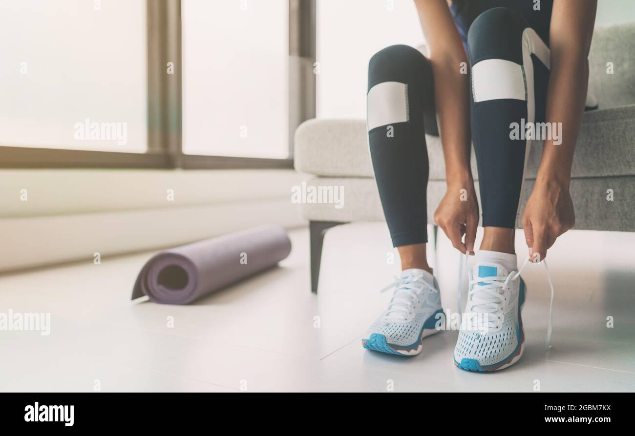 Woman tying running shoes laces getting ready to get back in shape going to yoga or pilates fitness class training at home Stock Photo