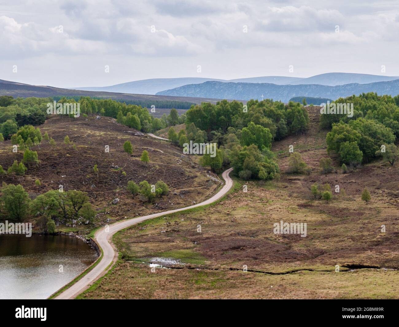 A narrow country lane winds through moorland hills under the mountains of the Highlands of Scotland. Stock Photo