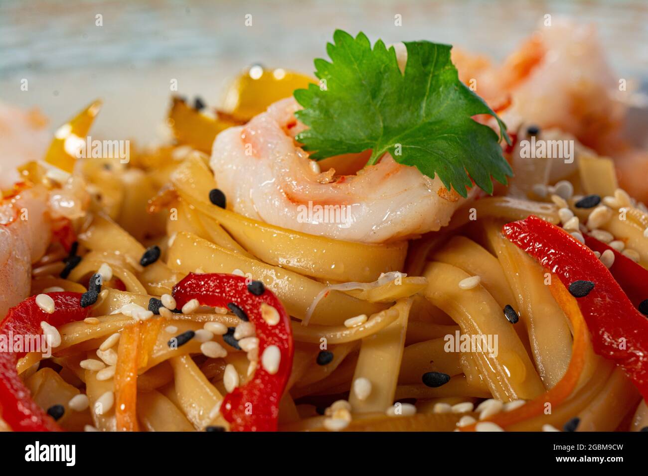 Udon noodles with fried shrimp, red onion and bell pepper, garnished with cilantro and sesame seeds. Traditional Asian cuisine. Stock Photo
