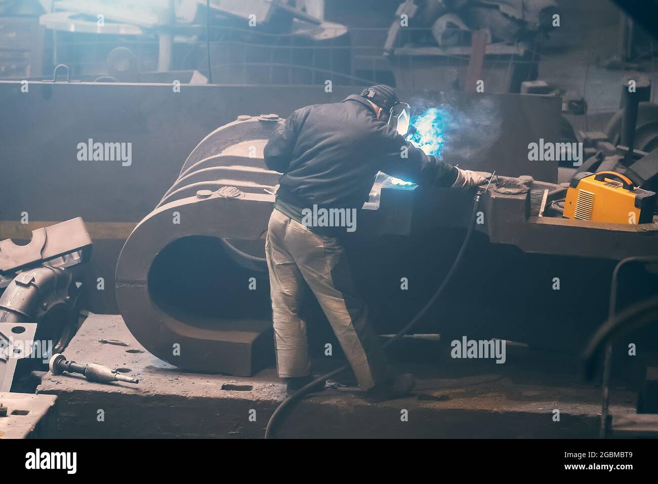 Welder processes large cast iron part in metallurgical plant after it has been melted or manufactured. Stock Photo
