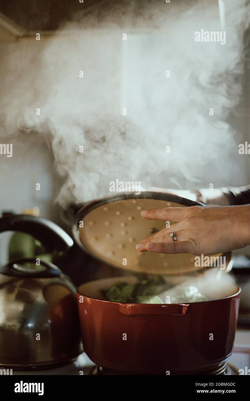 Vertical shot of a female hand taking off the pan lid and the steam coming out of it Stock Photo