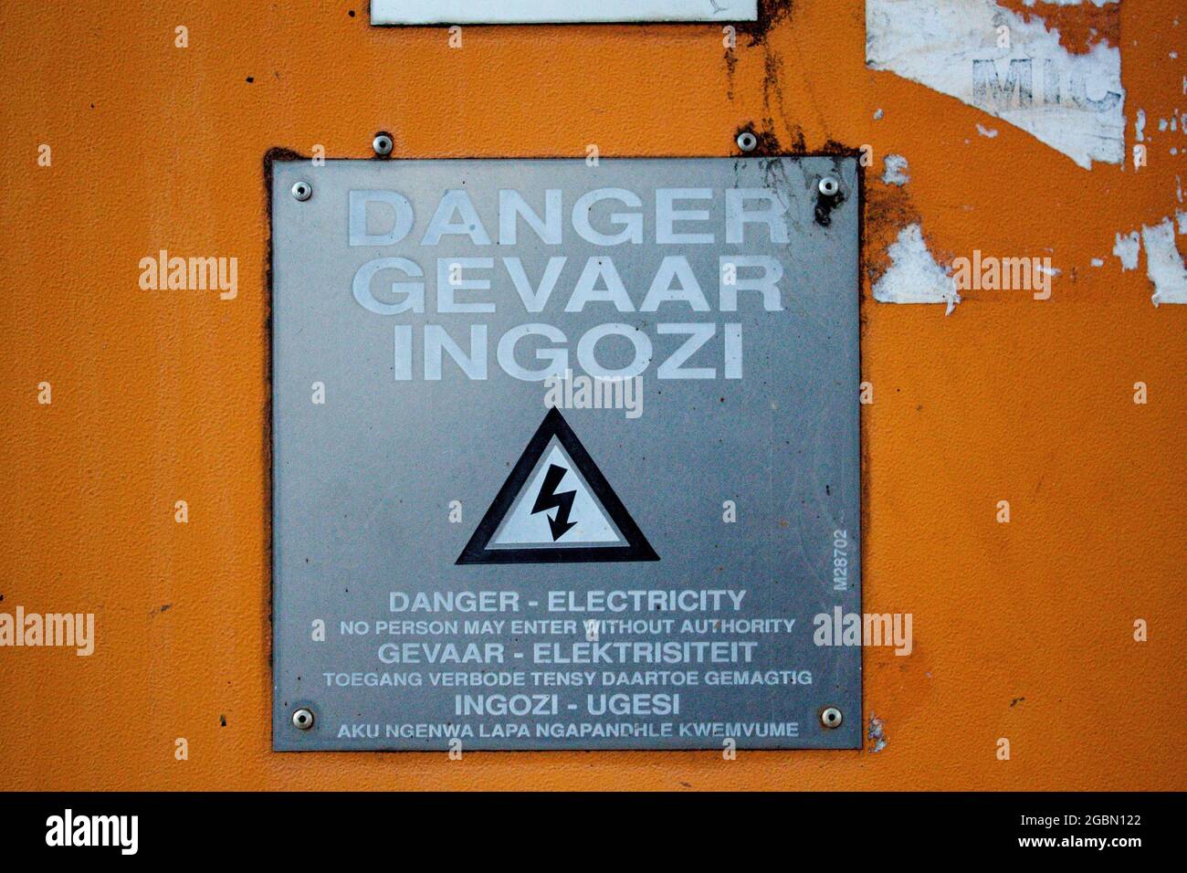 Warning sign with an electricity danger warning in English, Dutch, and Zulu on an orange wall Stock Photo
