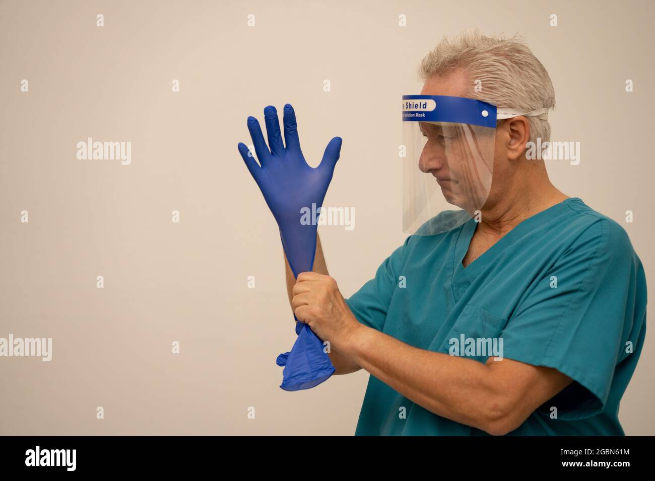 Doctor or nurse wearing a face shield mask and putting on blue latex gloves Stock Photo