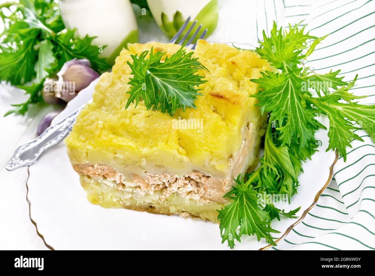 Mashed potato casserole with salmon fillet and lettuce in a plate, napkin, garlic on a white wooden board background Stock Photo