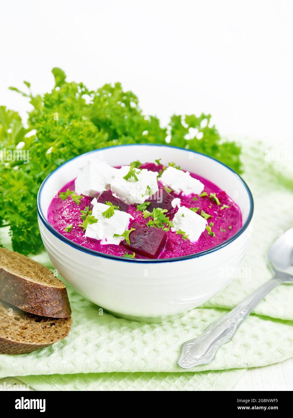 Soup puree of beetroot, potato and cream with salted cream cheese in a bowl on kitchen towel, bread and parsley on the background of light wooden boar Stock Photo
