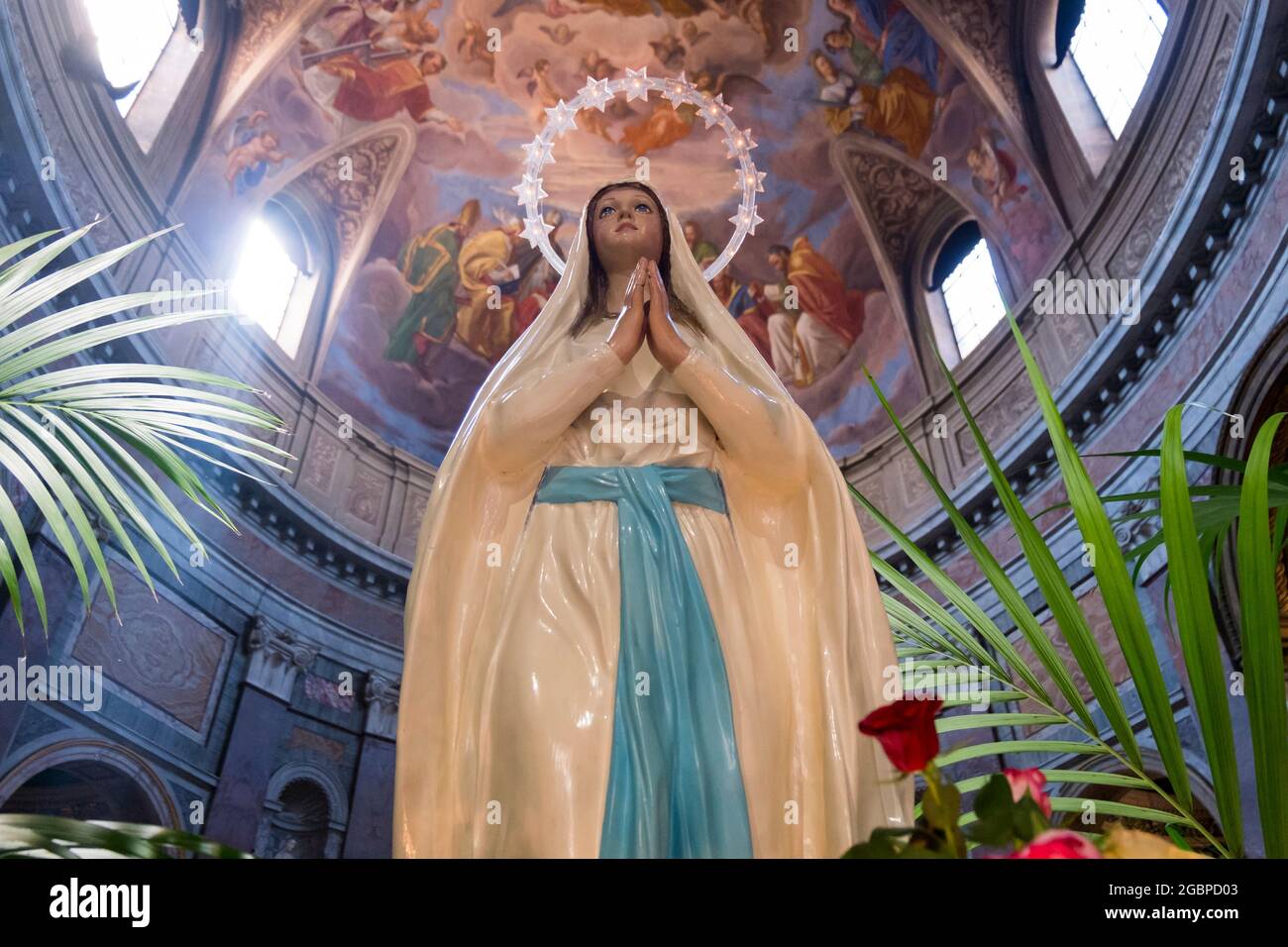 A sculpture, statue of the Virgin Mary, with white robe, blue sash and a lit halo. At a local church in Rome, Italy. Stock Photo