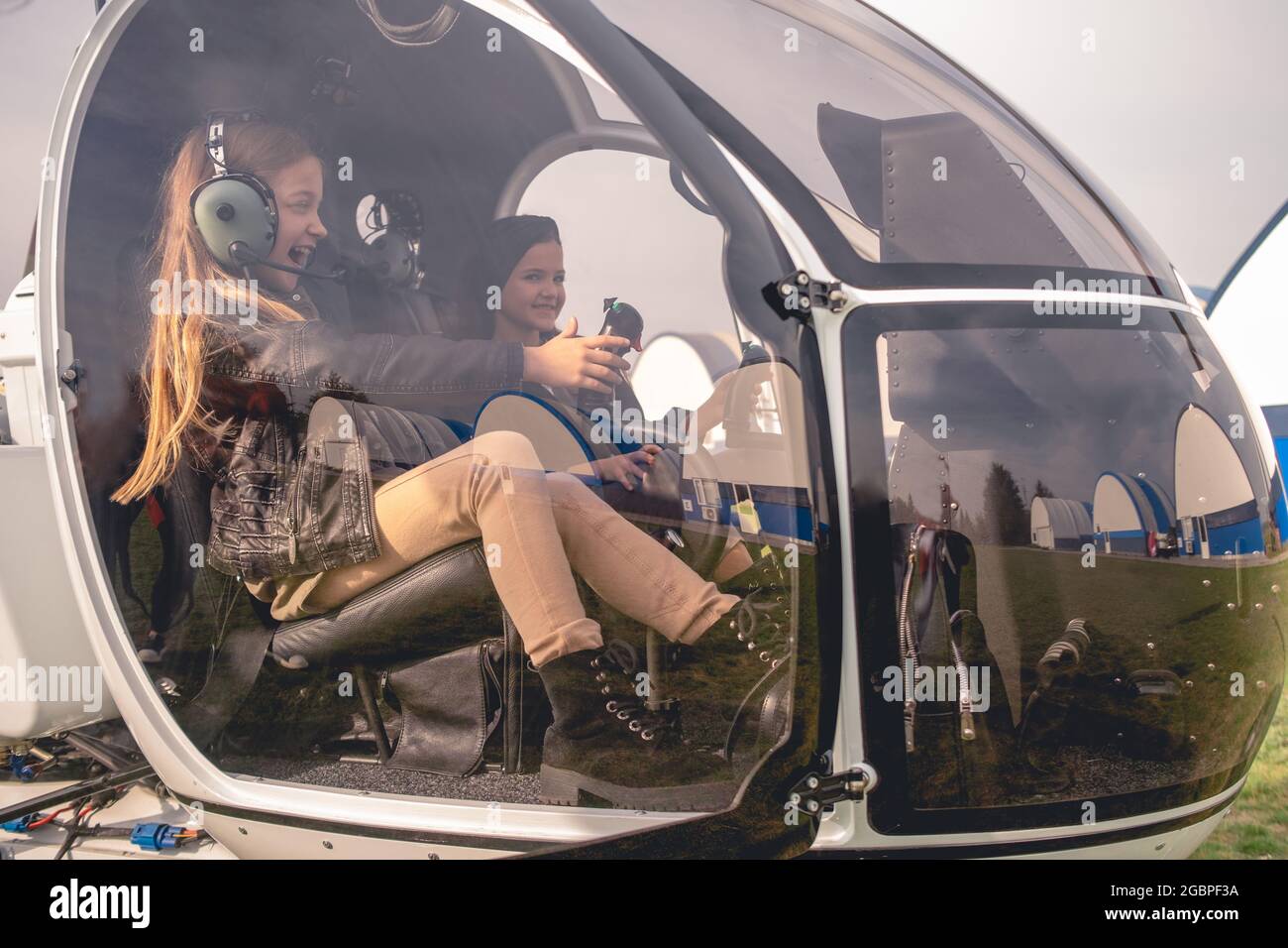 Excited tween girl in aviator headphones sitting in helicopter cockpit Stock Photo