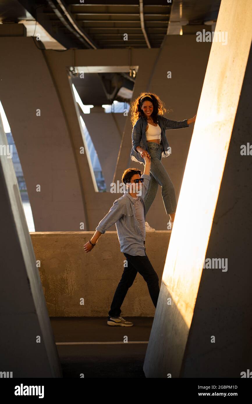 Trendy man and woman walk under bridge. Casual couple in street style clothes and trendy sunglasses Stock Photo