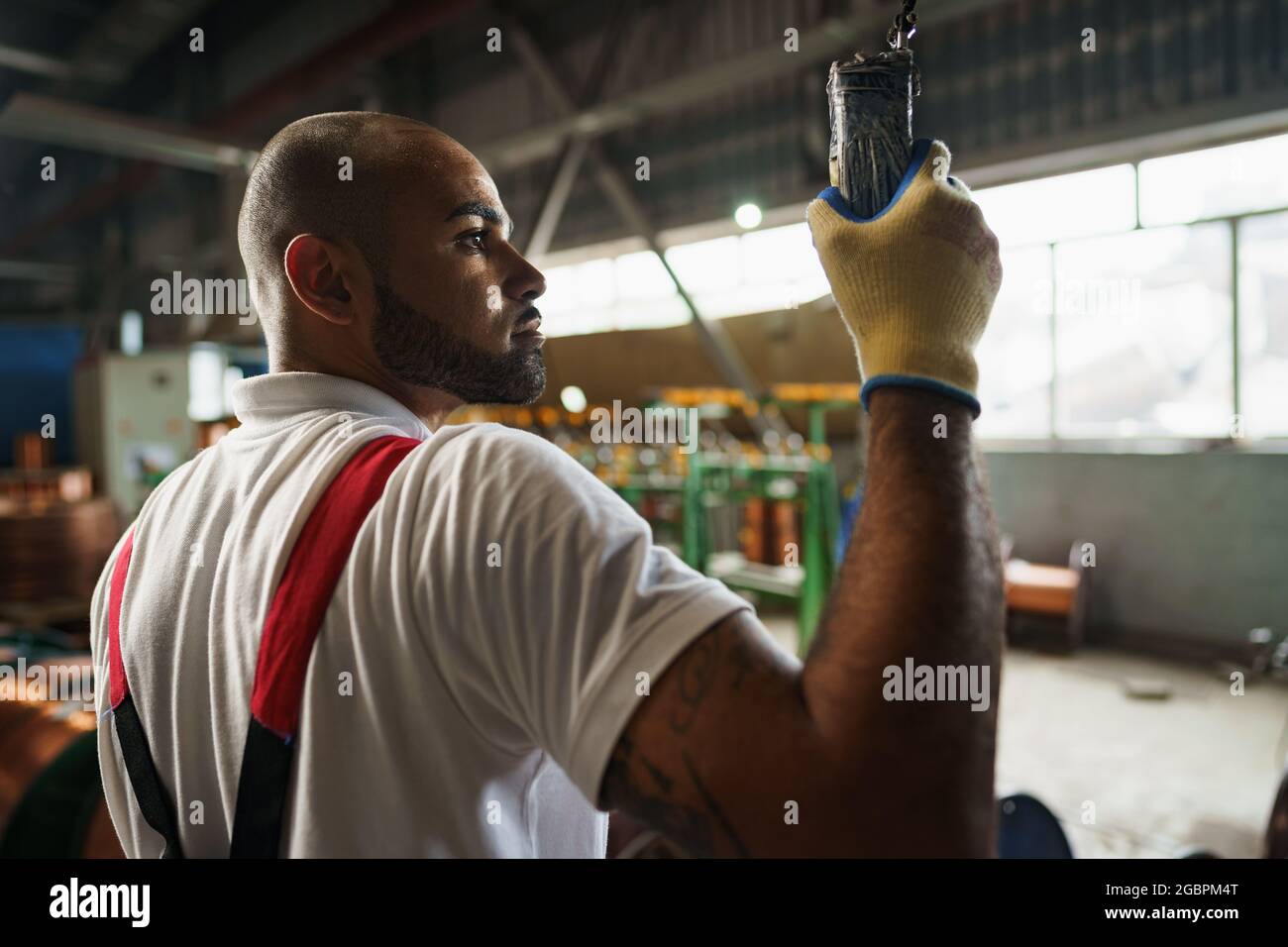 Engineer in uniform using crane controller hanging from ceiling in a factory Stock Photo