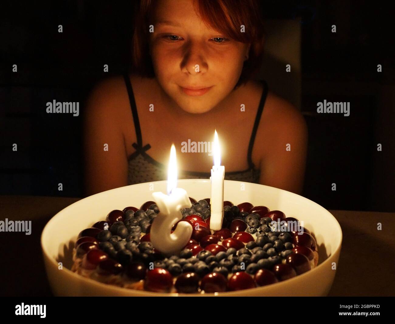 teenage girl pensively looks at burning candles 13 on a birthday cake in a dark room. Stock Photo