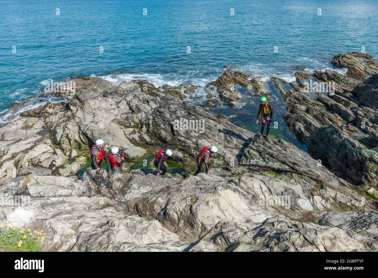 Holidaymakers and their guide walking across rocks on a coasteering adventure on Towan Head in Newquay in Cornwall. Stock Photo