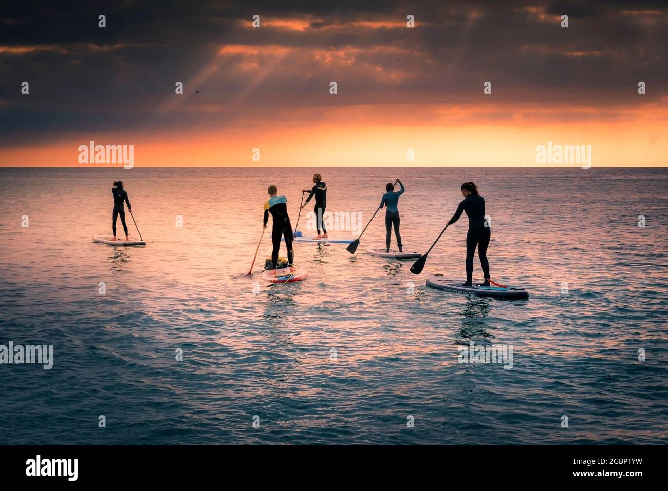 A group of Stand Up Paddleboarders setting out for an adventrous trip across Fistral Bay in evening light at Newquay in Cornwall. Stock Photo
