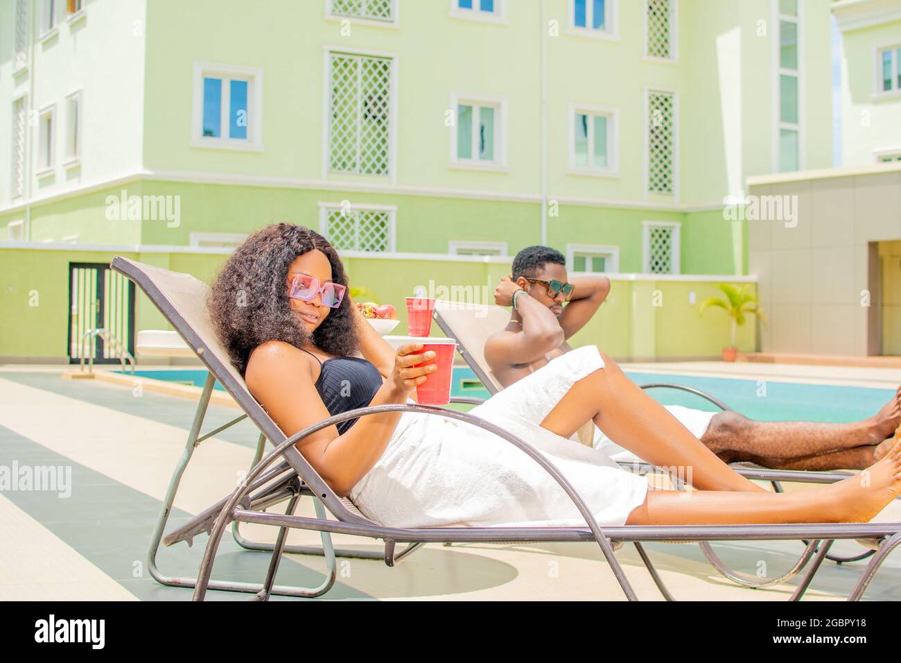 attractive young black woman relaxing by the pool alongside another guy. Stock Photo