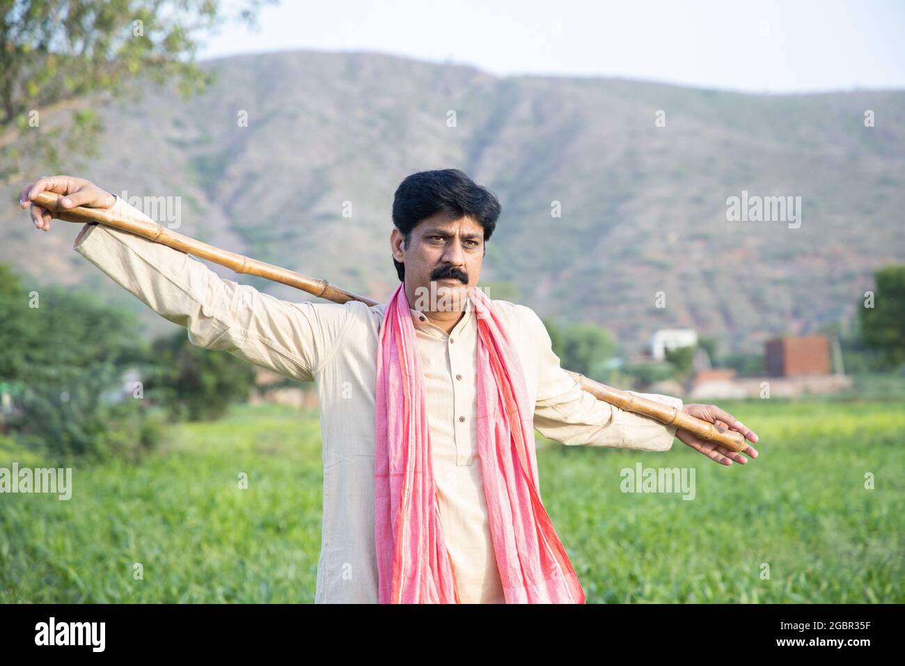 Indian farmer holding wood stick in hand standing in agriculture field ...