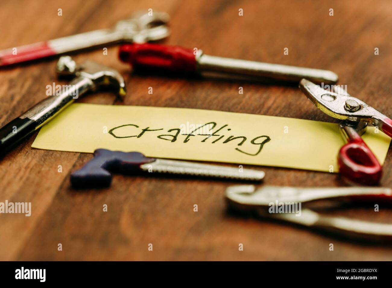 Crafting concept: Handwritten lettering 'crafting' on a sticky note surrounded by miniature crafting tools Stock Photo