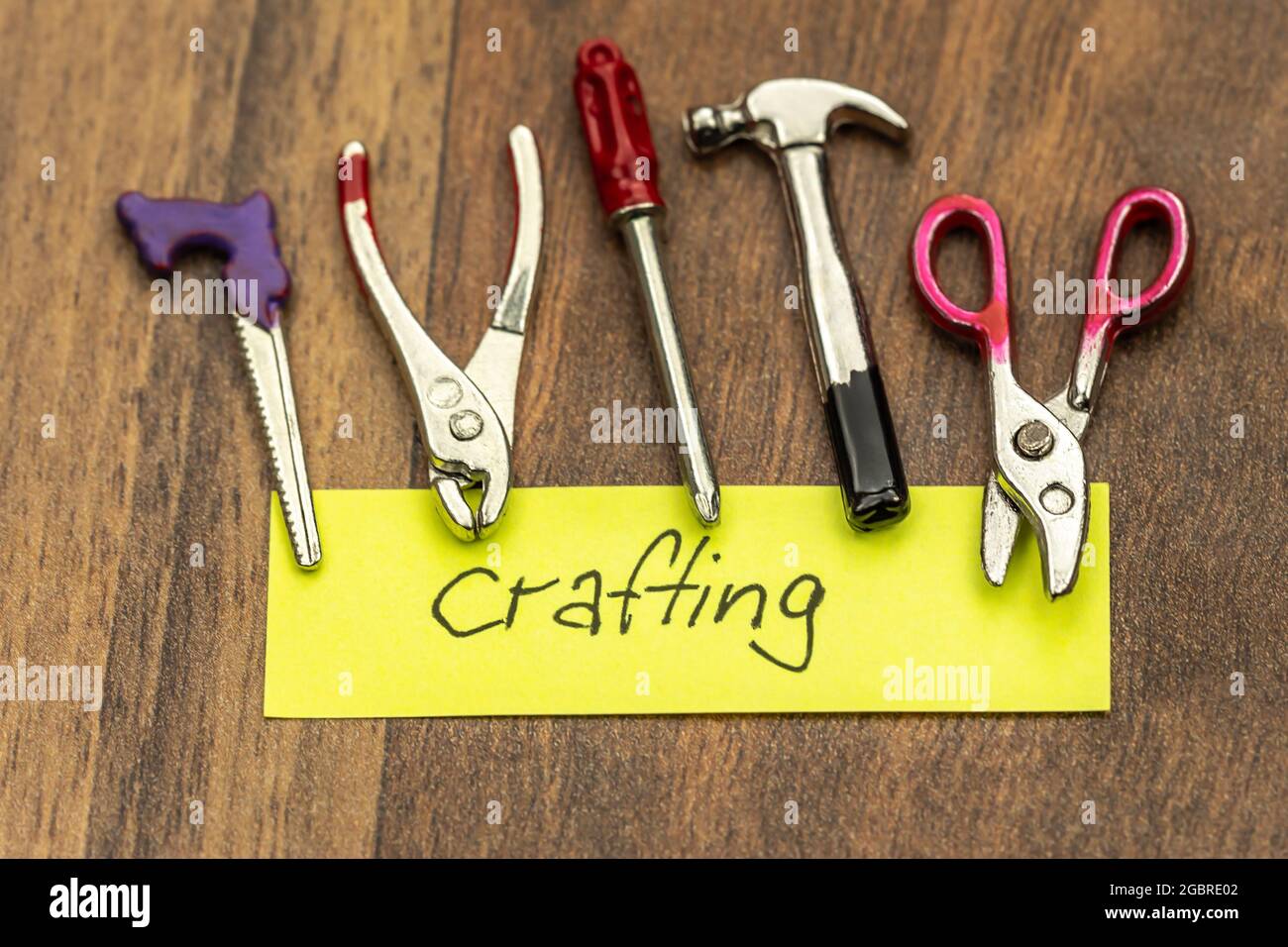 Crafting concept: Handwritten lettering 'crafting' on a sticky note surrounded by miniature crafting tools Stock Photo