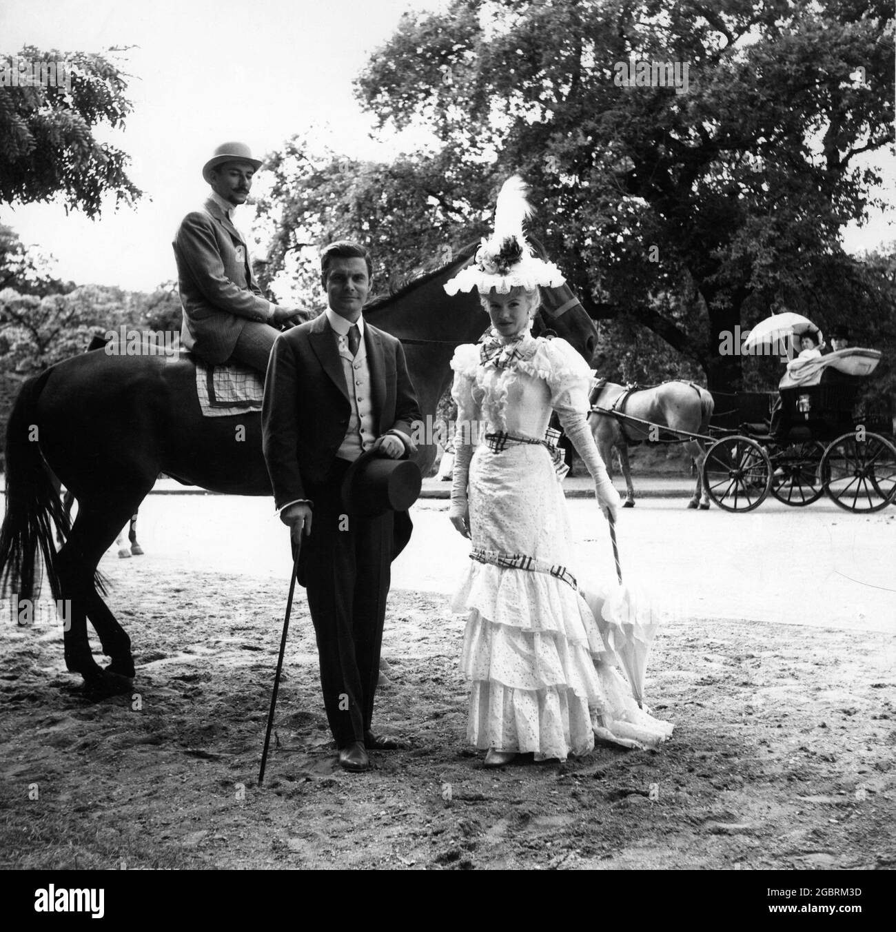LOUIS JOURDAN and Featured Extras modelling Costumes by CECIL BEATON on set during location filming in Paris of GIGI 1958 director VINCENTE MINNELLI based on novella by Colette screenplay / lyrics Alan Jay Lerner music Frederick Loewe production design / costumes Cecil Beaton producer Arthur Freed Metro Goldwyn Mayer Stock Photo