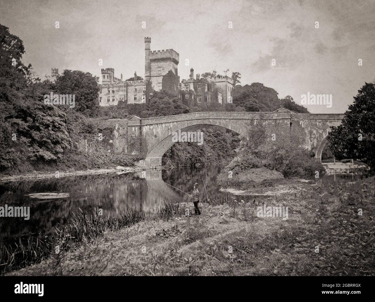 A late 19th century view of an angler by the River Blackwater in Lismore, County Waterford, Ireland. Behind is the Cavendish Bridge, aka Lismore Bridge built in 1858. Towering above both is  Lismore Castle, home of the Duke of Devonshire. It was largely re-built for William George Spencer Cavendish, 6th Duke of Devonshire, in the Gothic style by the architect William Atkinson from 1812 to 1822. In 1850 the 6th Duke engaged his architect Sir Joseph Paxton, the designer of The Crystal Palace, to carry out improvements and additions to the castle. Stock Photo
