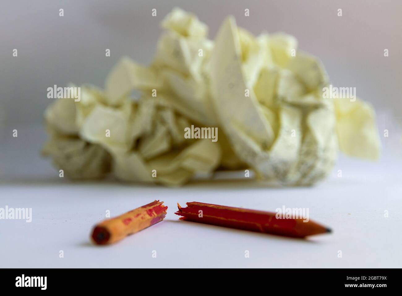 A chewed pencil lies snapped in two in front of out of focus screwed up paper, suggesting writers block. Horizontal format, neutral background. Stock Photo