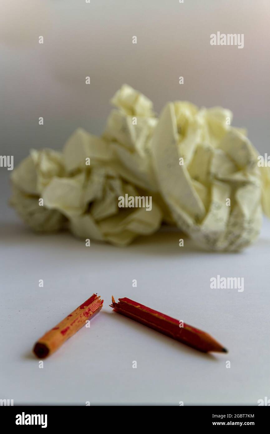 A chewed pencil lies snapped in two in front of some screwed up paper, suggesting writers block. Vertical format, neutral background, space for text Stock Photo