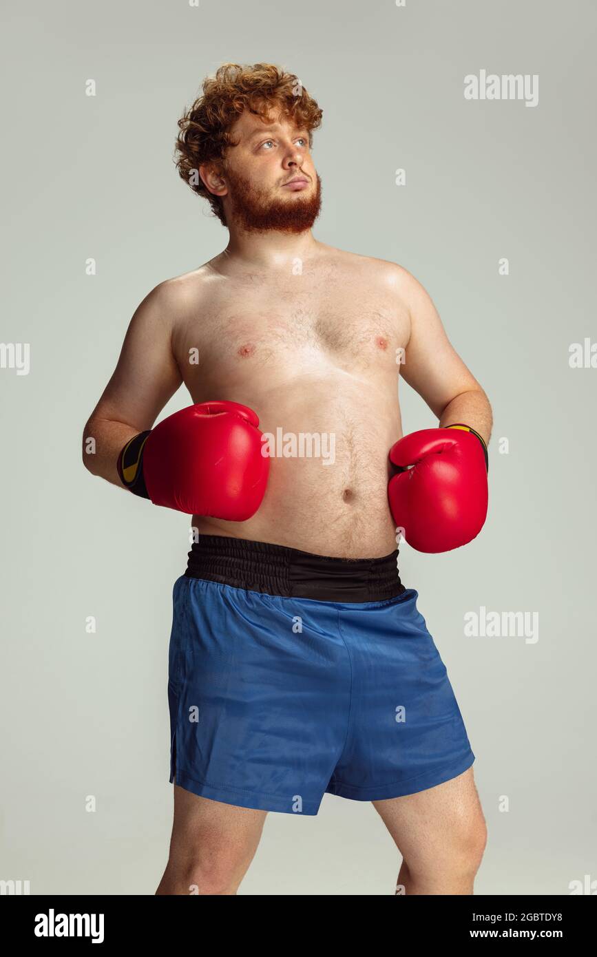 Funny redheaded man in blue boxing shorts and gloves isolated on gray