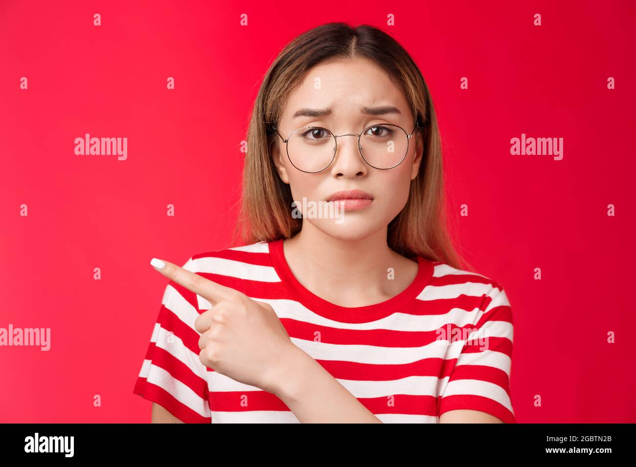 Sad cute asian female coworker tired working wear glasses frowning, pointing left look camera
