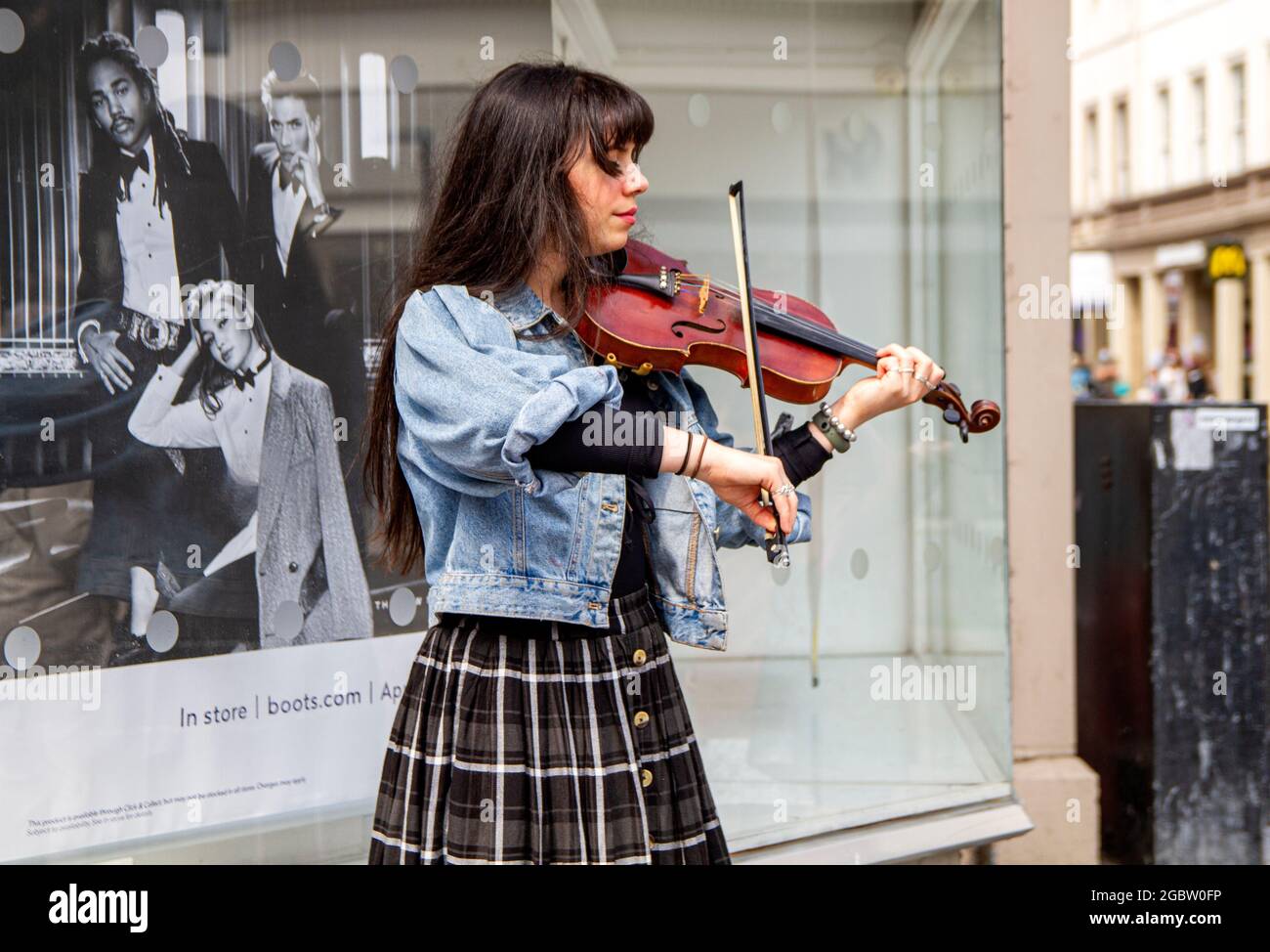 Dundee, Tayside, Scotland, UK. 5th Aug, 2021. UK Weather: A bright and windy day with sunny spells across North East Scotland with temperatures reaching 20°C. A young female violinist playing classical music whilst busking in the wind outside Boots the Chemist in Dundee city centre. Credit: Dundee Photographics/Alamy Live News Stock Photo