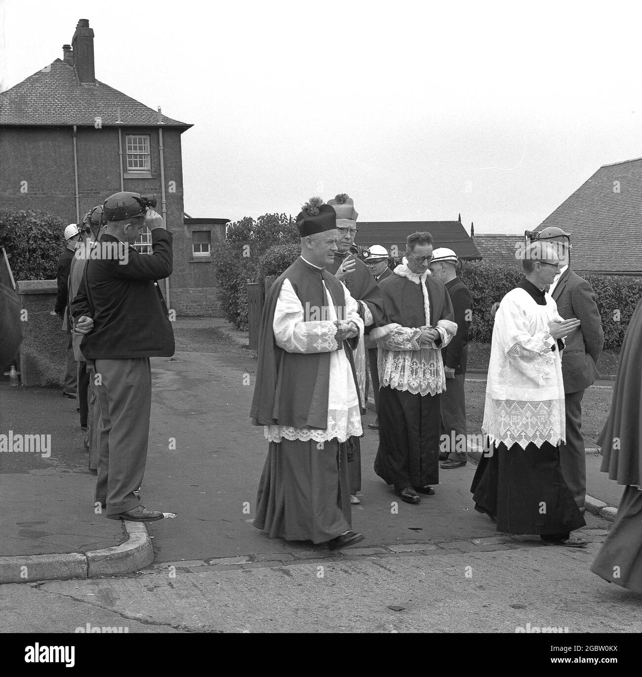 1960s, historical, Mine workers wearing their pit helmets standing in a line as a mark of respect to the Church of Scotland priests as they walk by, to perform a consecration at the local church, Lochgelly, Fife, Scotland, UK. The town had been a mining town since the early 1800s. Stock Photo