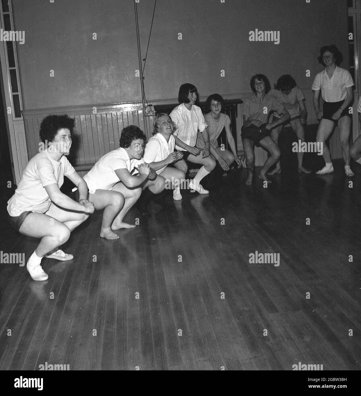 1960s, historical, inside the sports hall at a youth club, a group of teenage girls in their PE kits doing stretching or squatting exercises, Kelty, Scotland, UK. Stock Photo