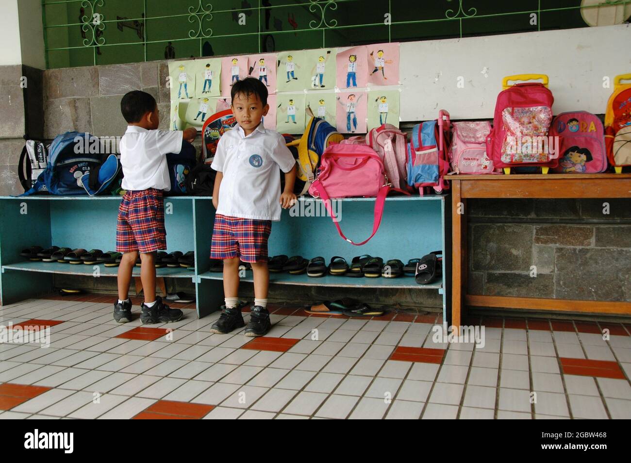 Two kindergarten students stand beside the bags and shoes shelf outside their classroom. Stock Photo