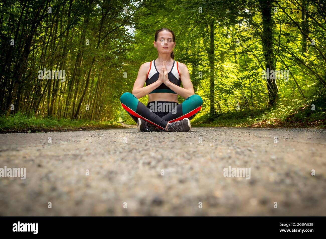 Woman meditating in a yoga pose sitting in the middle of a track in a ...