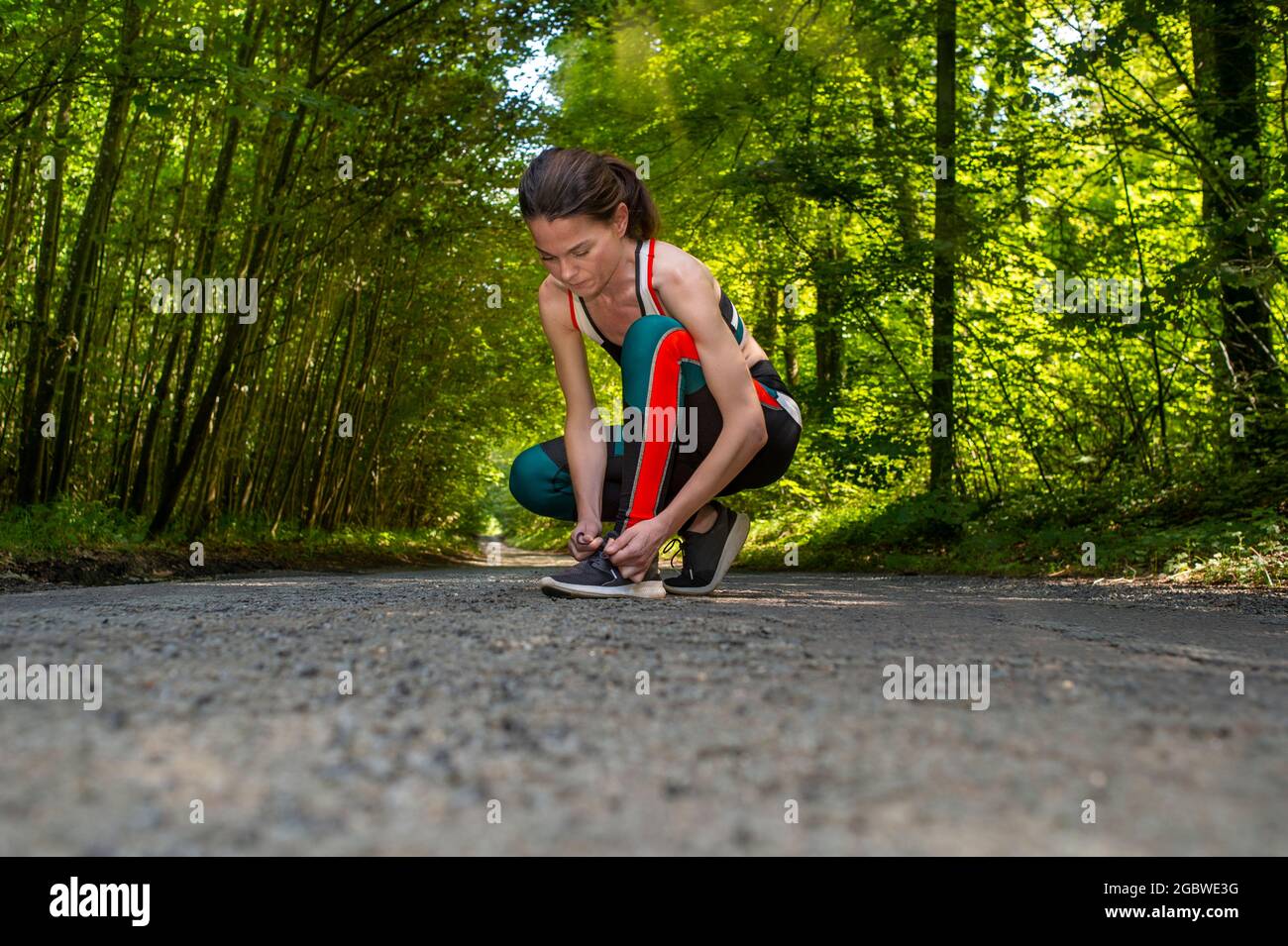 Woman runner tying shoelaces before jogging in autumn tree alley