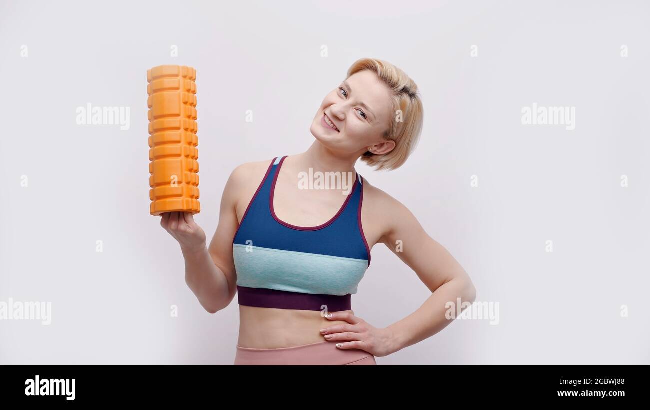 Girl holding a foam roller in her hand smiling. Cute girl ready for a  workout wearing a sports bra. Isolated over white background. Roller  fascia. Fitness and healthy lifestyle concept Stock Photo -