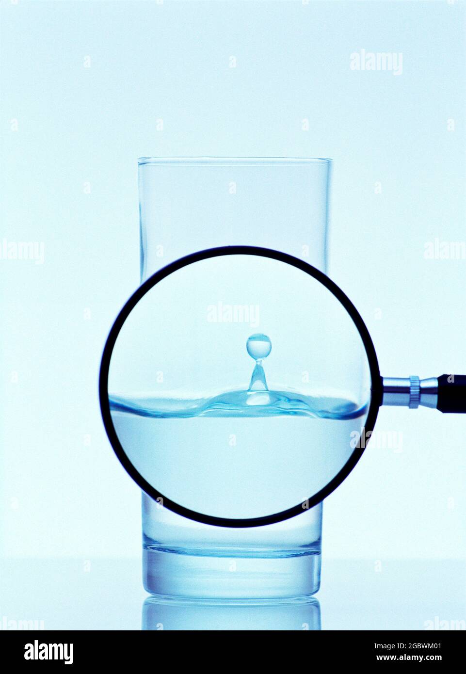 Magnifying glass view of water drop in a half filled glass of water