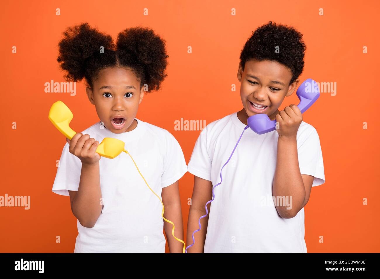 Photo of small impressed girl boy talk telephone wear white t-shirt isolated on orange background Stock Photo