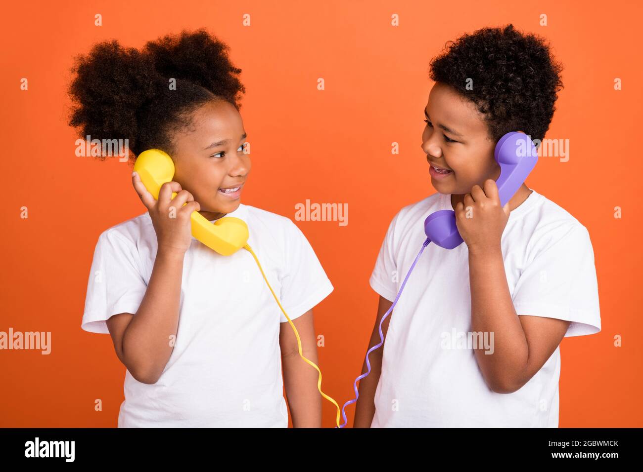 Photo of small funky girl boy talk telephone wear white t-shirt isolated on orange background Stock Photo