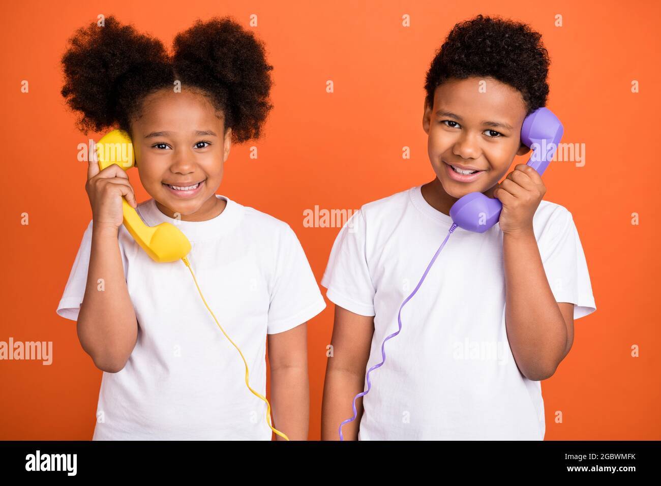 Photo of little funny girl boy talk telephone wear white t-shirt isolated on orange background Stock Photo