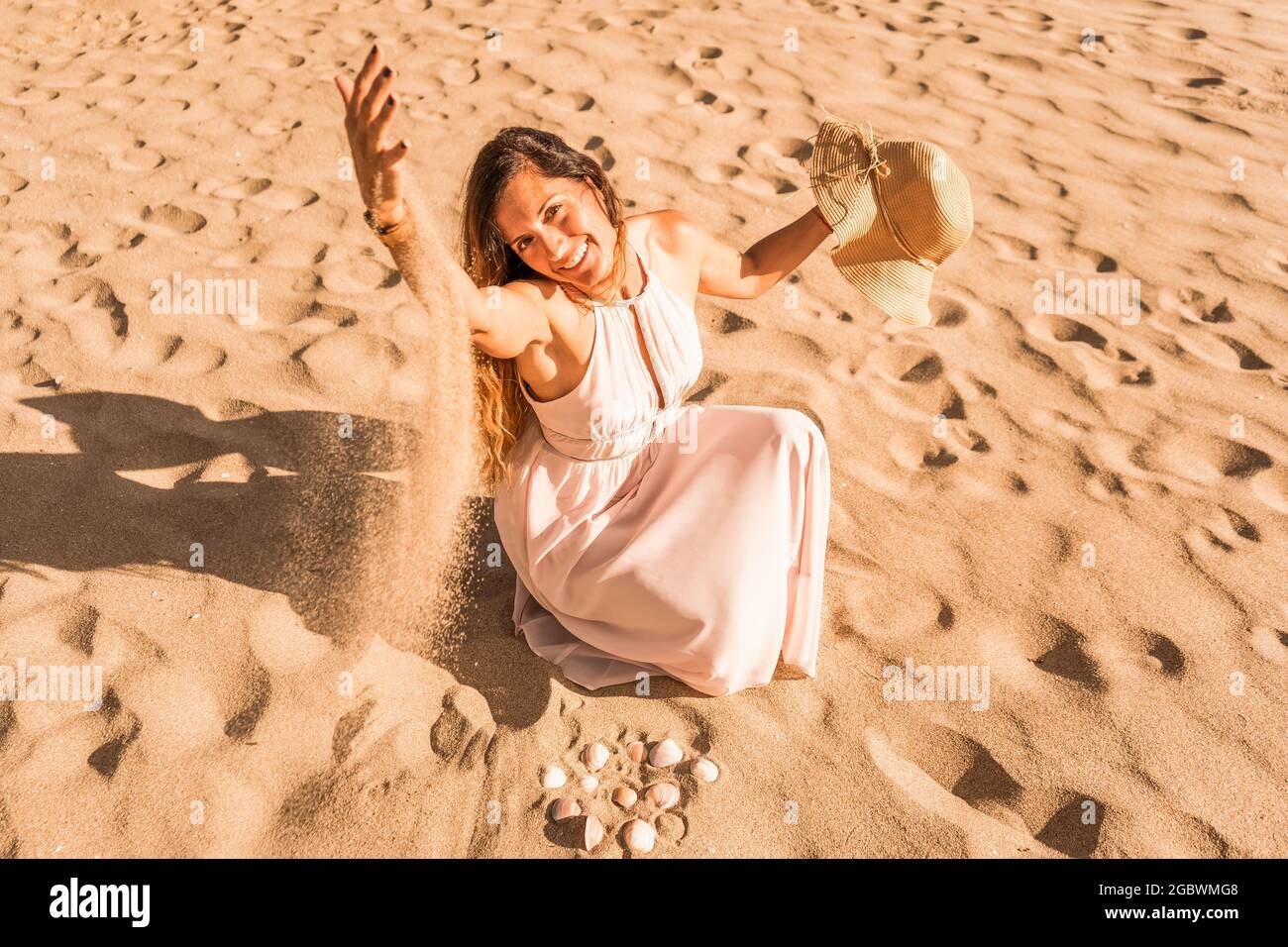 Beautiful caucasian woman in white dress sitting on the beach playing ...
